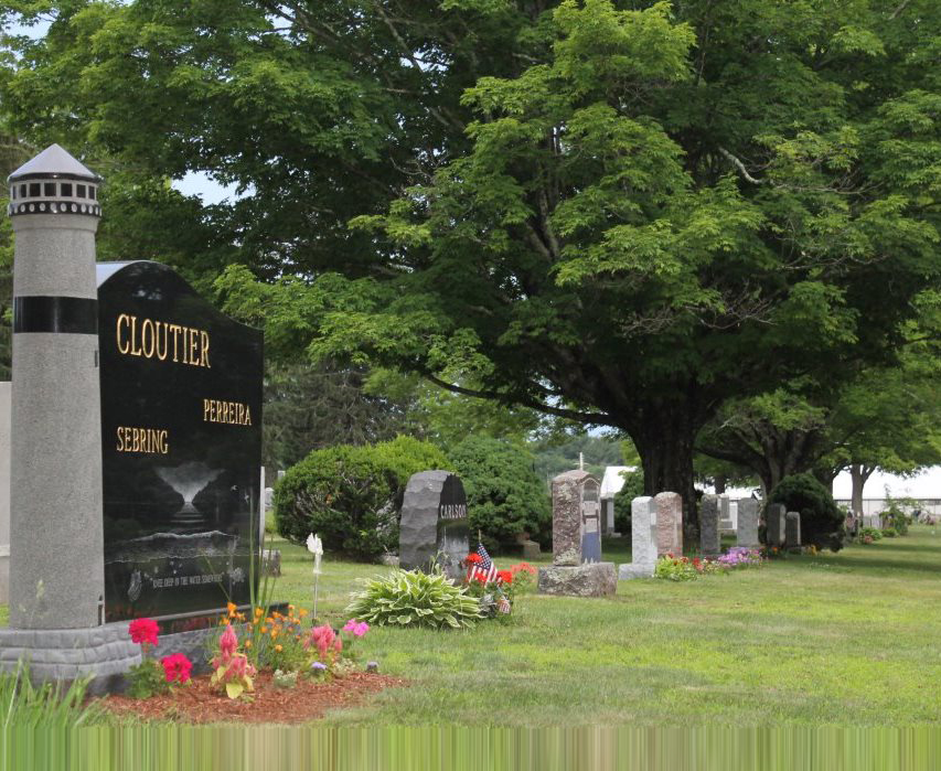 A black, lighthouse-shaped monument in a graveyard next to several other stones