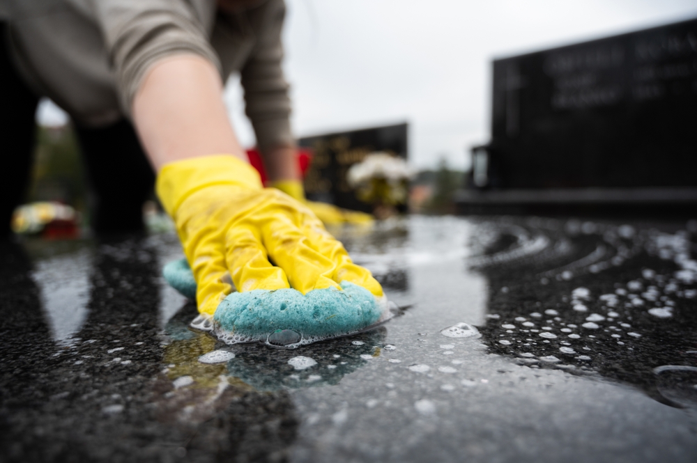 A black memorial being cleaned by a person with yellow gloves and a blue sponge